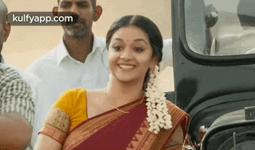 a woman in a saree is smiling while sitting in a car .