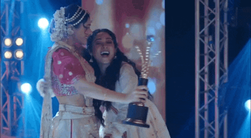two women are hugging each other on a stage while holding a trophy .