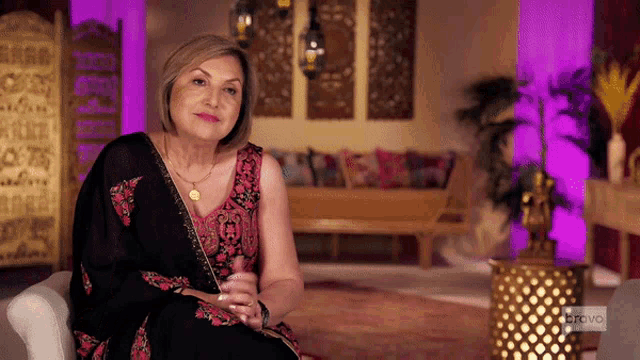 a woman is sitting in a living room with a bravo logo on the corner