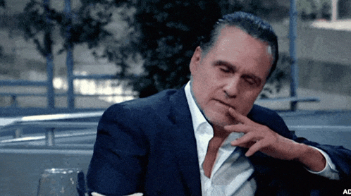a man in a suit and tie is sitting with his hand on his chin