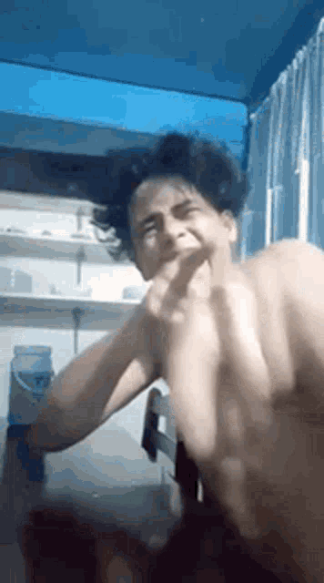 a shirtless man is making a funny face while sitting at a table in a room .