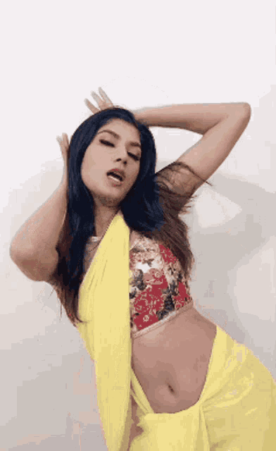 a woman wearing a yellow saree and a red floral blouse is dancing .