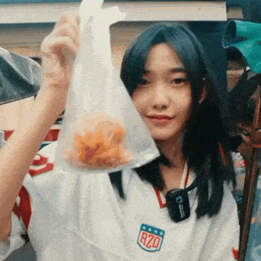a girl wearing a white rzq jersey holds a plastic bag of food