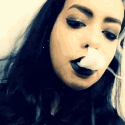 a woman with black lips is blowing a bubble with a cotton swab in her mouth .