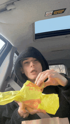 a person in a car holding a bag that says hot n spicy on it