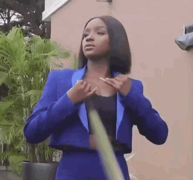 a woman in a blue suit is holding a hose and adjusting her jacket .