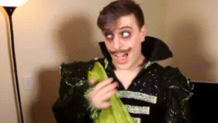 a man with a mustache is wearing a black and green costume and holding a green cloth .