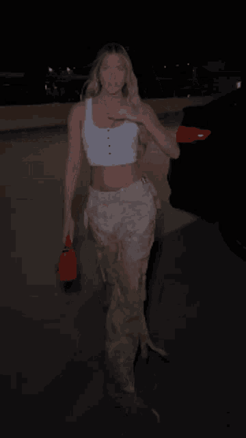 a woman in a crop top and pants is walking down a street at night