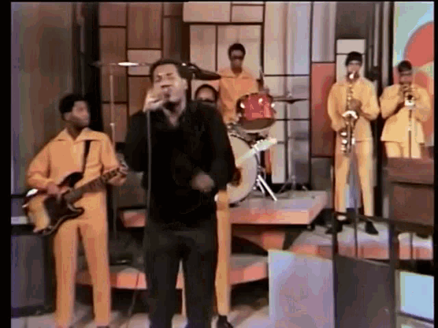 a man singing into a microphone in front of a band