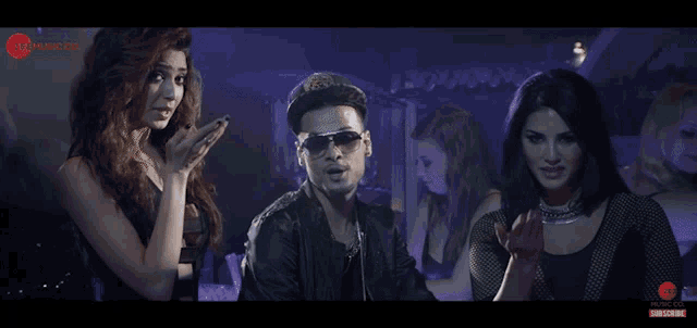 a man in a hat and sunglasses is surrounded by two women in a video for zee music
