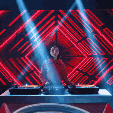 a woman in a red jacket is playing music on a turntable in front of a neon backdrop
