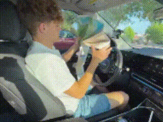 a man is sitting in the driver 's seat of a car eating a hamburger .