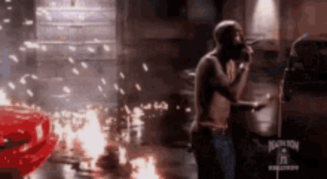 a man is singing into a microphone while a car is on fire in the background .
