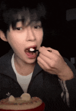 a young man is eating a piece of cake with a spoon in his mouth .