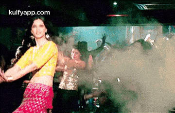 a woman in a yellow top is dancing in front of a crowd in a club .