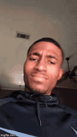 a man in a black hoodie is making a funny face while standing in front of a ceiling fan .