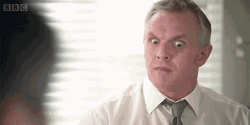 a man in a white shirt and tie is making a funny face while looking at another man .