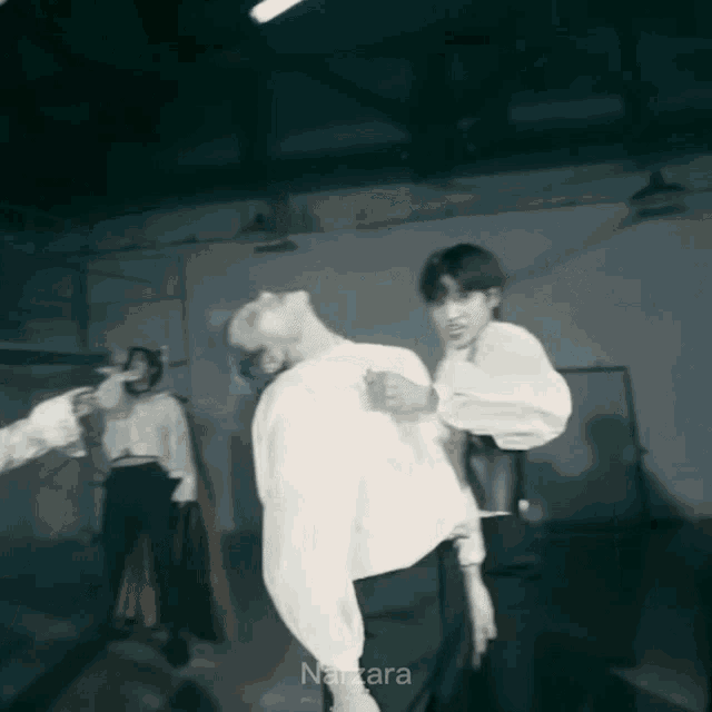 a man in a white shirt is standing next to another man in a dark room with the name nara on the bottom