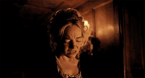 a woman is making a face in a dark room with a candle in the background .