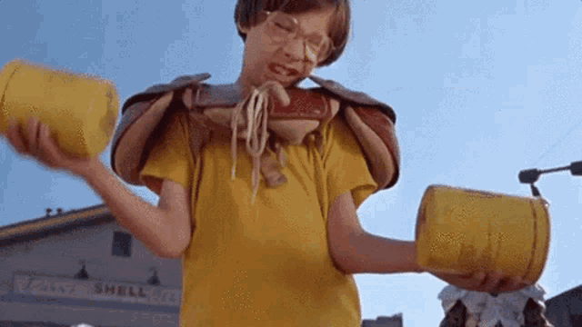 a boy in a yellow shirt is holding two yellow cans in front of a shell store