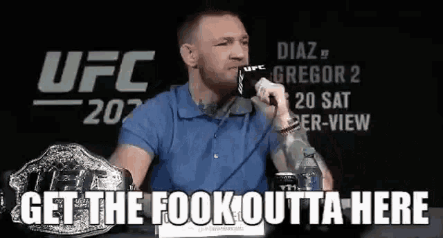 a man in a blue shirt is sitting at a table holding a microphone and talking into it .