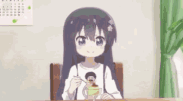 a girl with long black hair is sitting at a table with a spoon in her mouth .