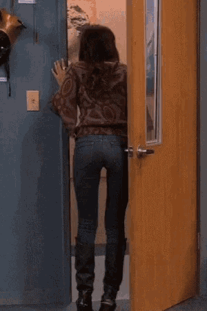 a woman in a leather jacket and jeans is standing in front of a wooden door .