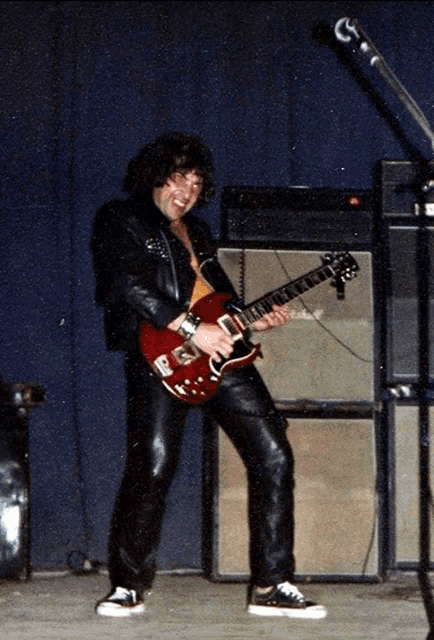 a man in a leather jacket is playing a red guitar on stage