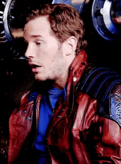 a man wearing a red leather jacket and a blue shirt looks surprised