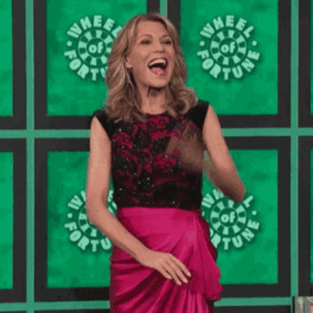 a woman in a pink skirt is waving in front of a wheel of fortune sign