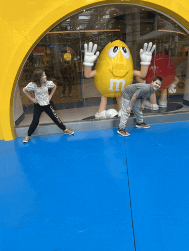 a boy and a girl standing in front of a yellow m & m statue