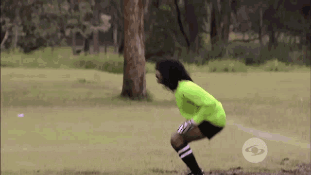a woman in a green shirt and black shorts is squatting on a soccer field