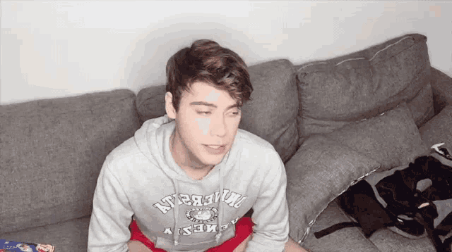 a young man is sitting on a couch wearing a grey sweatshirt that says abercrombie