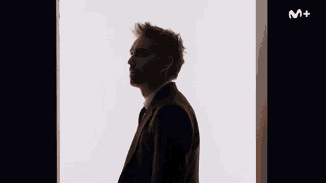 a man in a suit and tie is standing in front of a window with the letter m on it