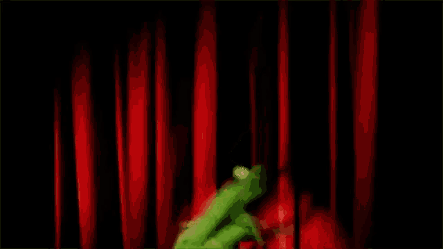 kermit the frog is dancing in front of a red curtain on a stage .