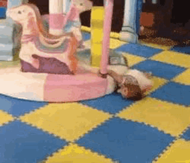 a child is laying on the floor next to a carousel horse .