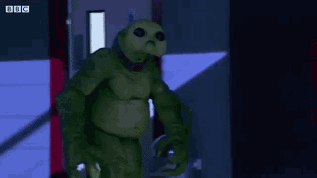a green alien is standing in a dark room next to a toilet .