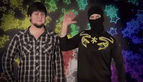 a man wearing a black mask stands next to another man wearing a shirt that says ' snake ' on it