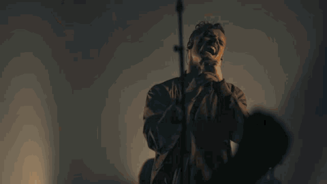 a man with a beard is singing into a microphone while another man stands behind him