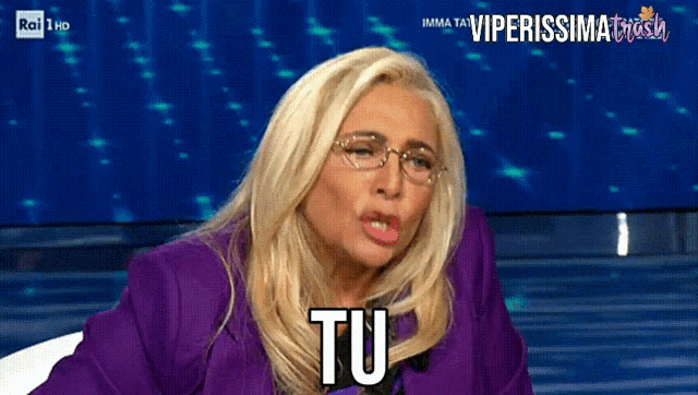 a woman wearing glasses and a purple jacket is pointing at the viewer