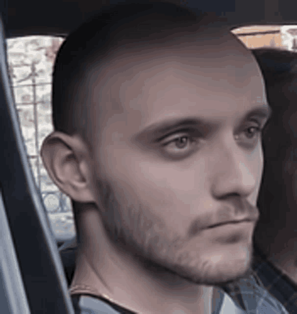 a bald man with a beard is sitting in a car and looking out the window .