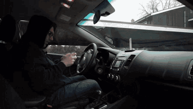 a man in a hooded sweatshirt is sitting in the driver 's seat of a car looking at his phone