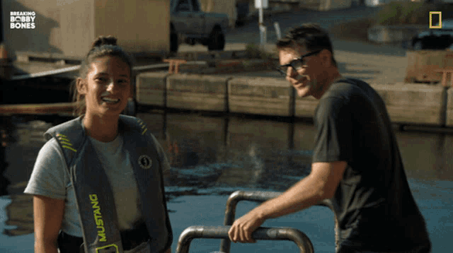 a woman wearing a mustang life vest smiles next to a man in glasses