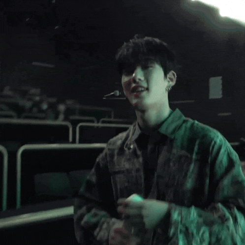 a man in a camouflage shirt sits next to another man in a white shirt in a dark room