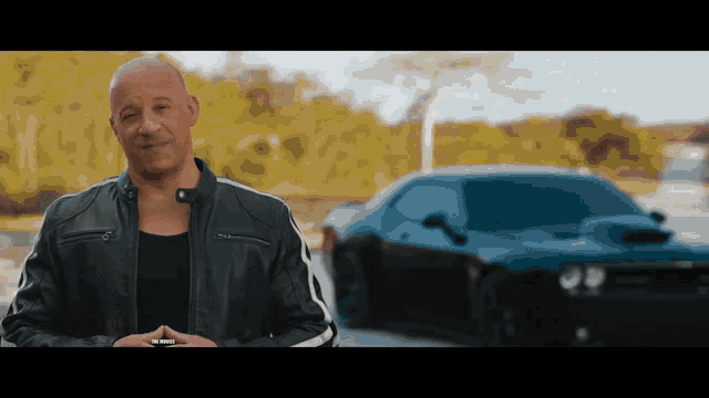 a man in a black leather jacket is standing in front of a blue car