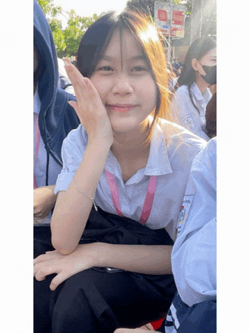 a girl wearing a white shirt with a pink ribbon around her neck is smiling for the camera while sitting in a crowd of people