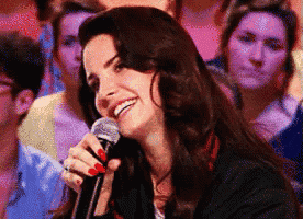 a woman with red nails is singing into a microphone and smiling