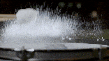 a drum is being smashed with a mallet and a lot of water is coming out of it