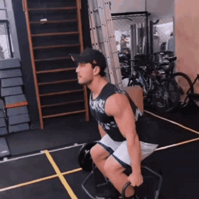 a man wearing a hat is squatting with a barbell in a gym .