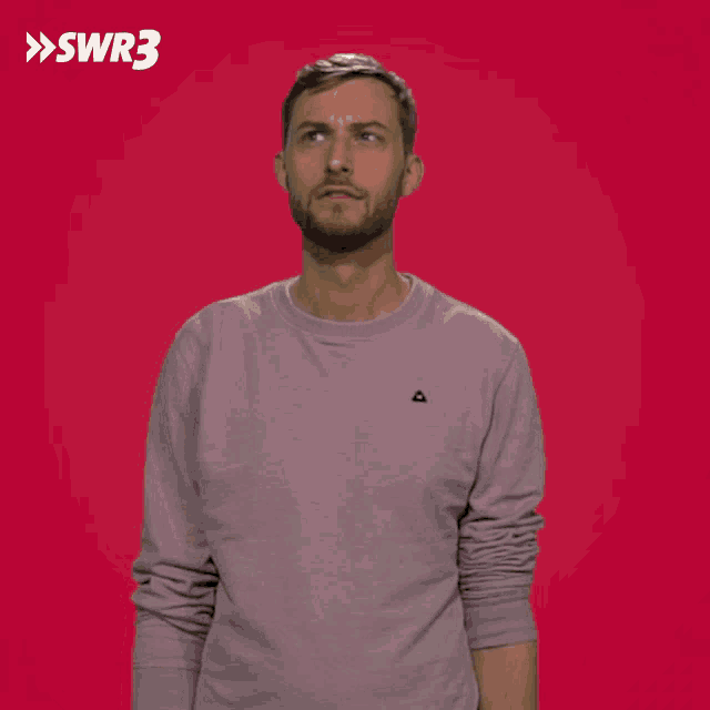 a man wearing a pink sweater with a black triangle on the chest looks up at the sky